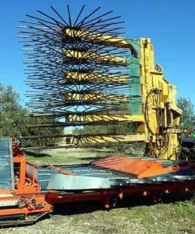 Olive harvesting machine with a large rake attachment and a tractor in a field. - Olive Oil Times