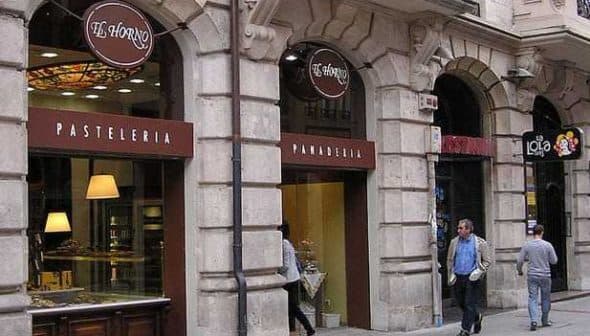 Facade of a pastry shop and bakery with signs in Spanish, featuring glass display windows. - Olive Oil Times