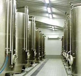 Row of stainless steel storage tanks in an industrial facility with pipes and valves. - Olive Oil Times