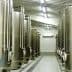 Row of stainless steel storage tanks in an industrial facility with pipes and valves. - Olive Oil Times