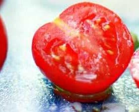 A halved tomato showing its interior with seeds and flesh visible on a reflective surface. - Olive Oil Times