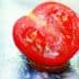 A halved tomato showing its interior with seeds and flesh visible on a reflective surface. - Olive Oil Times