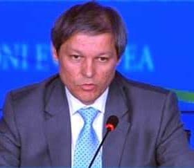 A man in a suit speaking at a podium during a conference with a blue backdrop. - Olive Oil Times