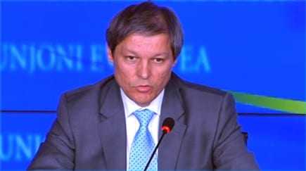 A man in a suit speaking at a podium during a conference with a blue backdrop. - Olive Oil Times