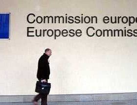 A person walking past the European Commission signage with the EU flag displayed on the wall. - Olive Oil Times