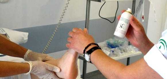 Medical professional applying a spray treatment to a patient's leg in a clinical setting. - Olive Oil Times