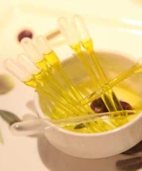 A small white bowl containing yellow oil and several clear pipettes arranged inside it. - Olive Oil Times