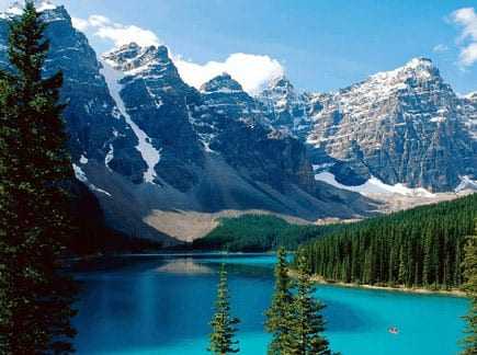 A scenic view of a mountain lake surrounded by pine trees and rocky peaks under a blue sky. - Olive Oil Times
