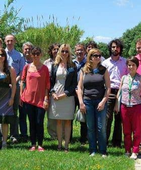 A group of diverse individuals posing together outdoors in a green area with trees and grass. - Olive Oil Times