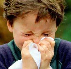 A young boy holding a tissue to his nose while sneezing outdoors. - Olive Oil Times