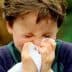 A young boy holding a tissue to his nose while sneezing outdoors. - Olive Oil Times