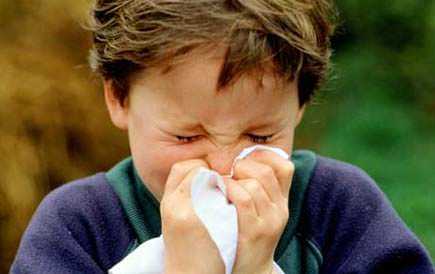A young boy holding a tissue to his nose while sneezing outdoors. - Olive Oil Times