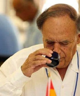 An older man in a white shirt tasting olive oil from a small glass cup. - Olive Oil Times