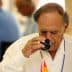An older man in a white shirt tasting olive oil from a small glass cup. - Olive Oil Times