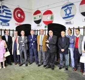 A group of individuals standing in a meeting room with flags displayed on the wall behind them. - Olive Oil Times