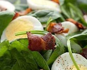A bowl of salad containing spinach, sliced hard-boiled eggs, and pieces of bacon. - Olive Oil Times