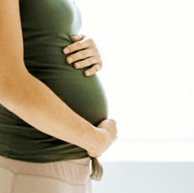 Side view of a pregnant woman in a green top gently holding her belly with both hands. - Olive Oil Times