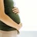 Side view of a pregnant woman in a green top gently holding her belly with both hands. - Olive Oil Times