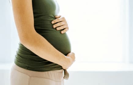 Side view of a pregnant woman in a green top gently holding her belly with both hands. - Olive Oil Times