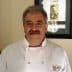 A chef wearing a white coat with a UC Davis logo, smiling in a well-lit indoor setting. - Olive Oil Times