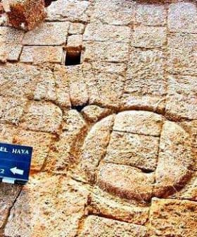 Excavated ancient stone structure featuring a circular stone element and a sign for reference. - Olive Oil Times