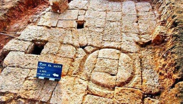 Excavated ancient stone structure featuring a circular stone element and a sign for reference. - Olive Oil Times