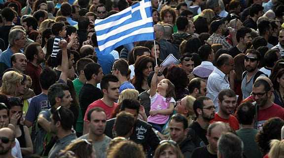A large crowd of people with a young girl holding a Greek flag in a public gathering. - Olive Oil Times