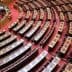 Interior view of the Greek Parliament chamber featuring rows of wooden seating and a red carpet. - Olive Oil Times