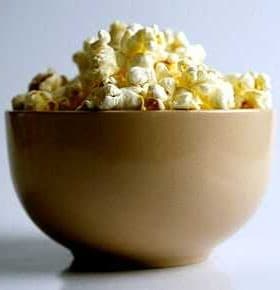 A beige bowl filled with freshly popped popcorn against a plain background. - Olive Oil Times