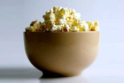 A beige bowl filled with freshly popped popcorn against a plain background. - Olive Oil Times
