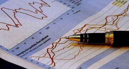 A pen resting on a sheet of paper with financial graphs and data trends. - Olive Oil Times