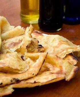 A plate of socca, a type of flatbread, with several bottles of olive oil in the background. - Olive Oil Times