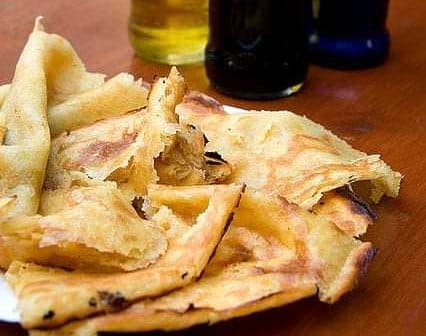 A plate of socca, a type of flatbread, with several bottles of olive oil in the background. - Olive Oil Times