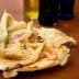 A plate of socca, a type of flatbread, with several bottles of olive oil in the background. - Olive Oil Times