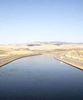 Irrigation canal running through a dry landscape in California with mountains in the background. - Olive Oil Times