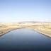 Irrigation canal running through a dry landscape in California with mountains in the background. - Olive Oil Times