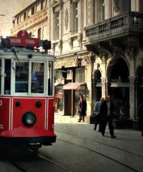 A red vintage tram traveling along a street in Istanbul with pedestrians nearby. - Olive Oil Times