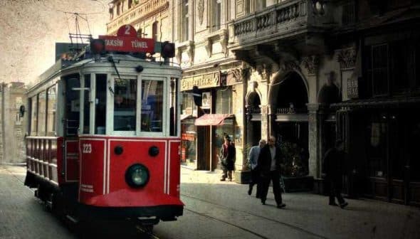 A red vintage tram traveling along a street in Istanbul with pedestrians nearby. - Olive Oil Times