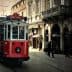 A red vintage tram traveling along a street in Istanbul with pedestrians nearby. - Olive Oil Times