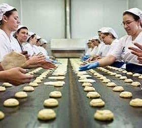Workers shaping dough into tortas on a production line in a bakery setting. - Olive Oil Times
