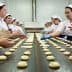 Workers shaping dough into tortas on a production line in a bakery setting. - Olive Oil Times