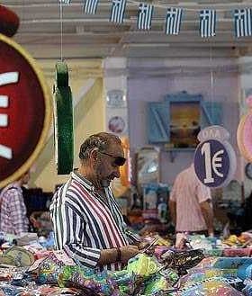 A market scene featuring price tags displaying '1€' and shoppers browsing various items. - Olive Oil Times