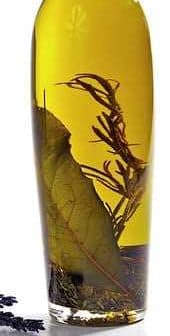 Bottle of infused olive oil containing herbs and leaves submerged in oil. - Olive Oil Times