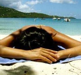 Individual lying face down on a beach towel on a sandy beach near the water. - Olive Oil Times