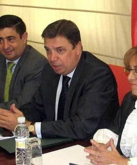 Four individuals seated at a table during a meeting, with one person speaking and others listening attentively. - Olive Oil Times