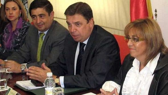 Four individuals seated at a table during a meeting, with one person speaking and others listening attentively. - Olive Oil Times