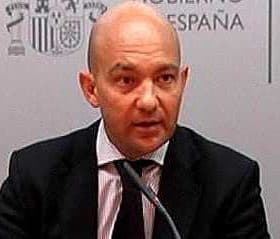 A man in a suit speaking at a press conference with a microphone in front of him. - Olive Oil Times