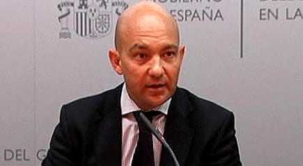 A man in a suit speaking at a press conference with a microphone in front of him. - Olive Oil Times