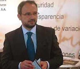 Man wearing glasses and a suit holding a document at a conference or event. - Olive Oil Times