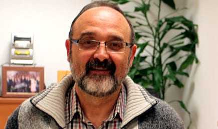 A man with glasses and a beard wearing a gray sweater, smiling in an indoor setting. - Olive Oil Times